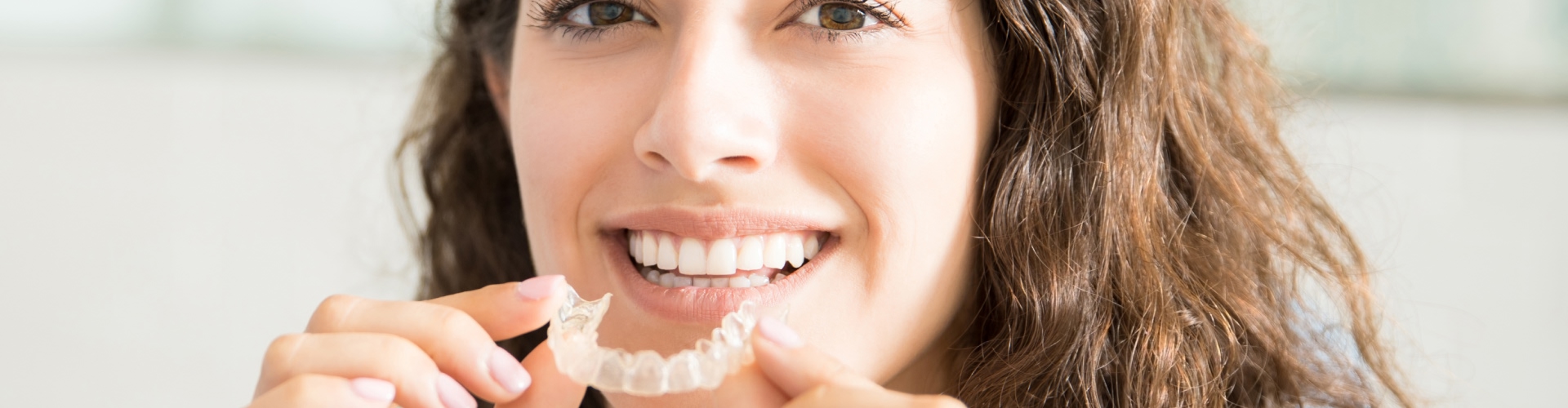 Smiling woman holding clear aligner in front of her mouth.